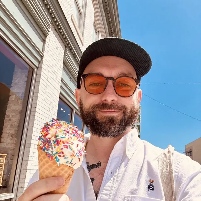 Blair in a black cap and orange-tinted sunglasses, holding an ice cream cone
